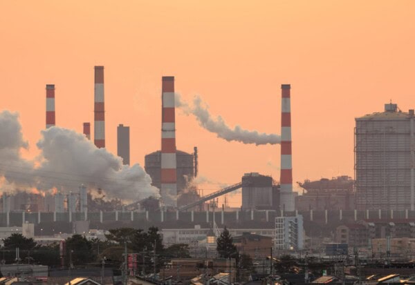 smoke rises from industrial plant with orange sunset glow in sky